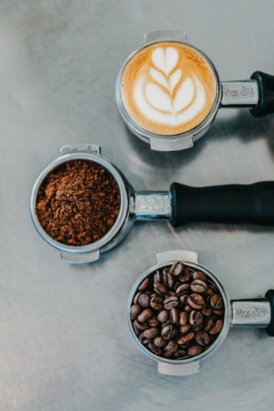 Espresso portafilters showing whole beans, fresh grounds and a finished latte